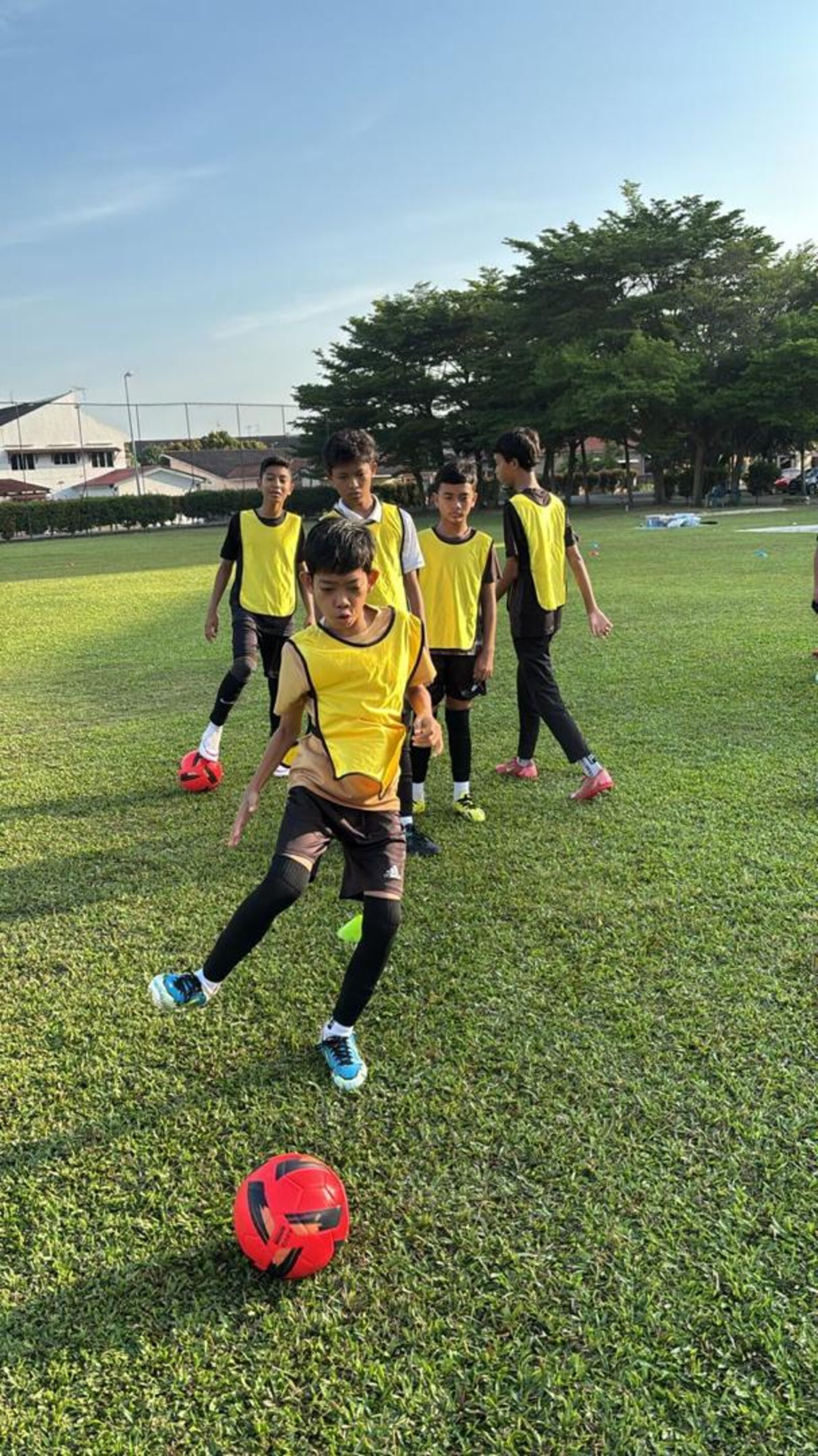 Sesi latihan pemain muda memakai vest oren dan biru di padang sekolah